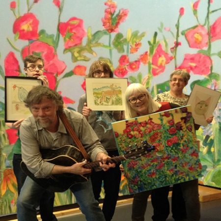 A group holding paintings in front of background of tall painted flowers