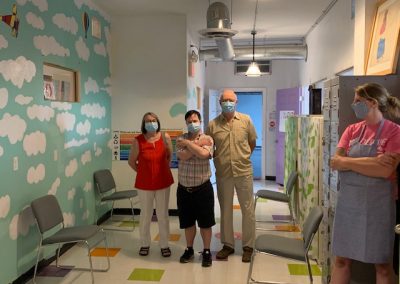 Masked artist and two family members in hallway with masked H'art staff