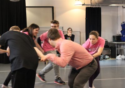 Dance group circles, choreographer watching