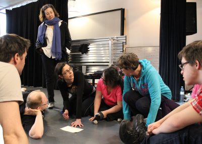 Creative team discusses while sitting on theatre floor