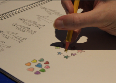 Hand holding yellow pencil crayon filling in a star under sketches of community helpers