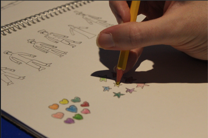 Hand holding yellow pencil crayon filling in a star under sketches of community helpers