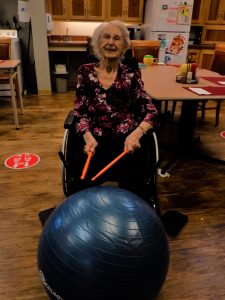 Seated woman holding drumsticks in front of a large ball. 