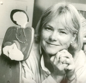 Photo portrait of Founder Katherine Porter, circa 1998. Smiling beside wood sculpture.