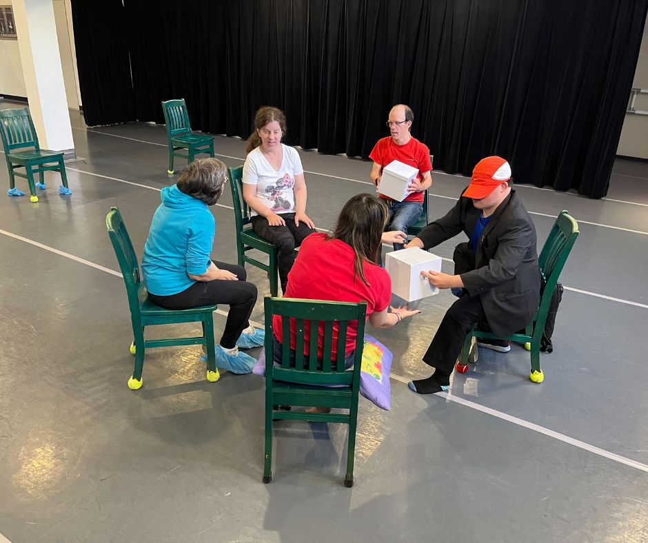 A group of five seated H'art artists pass two boxes around a circle