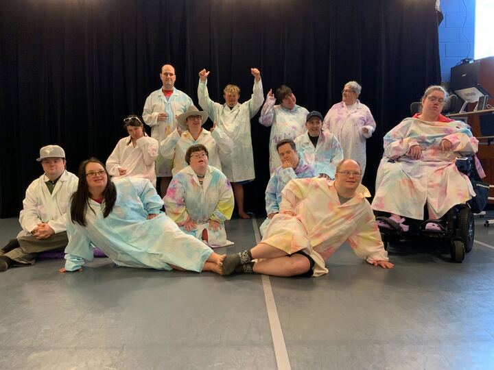 A group of about a dozen H'art artists posing in tie-dyed coats.